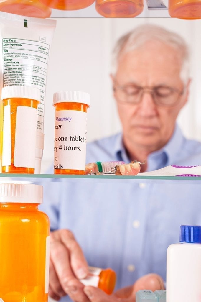 elderly man taking pain medicine in pharmacy cabinet